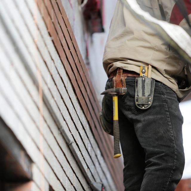 Tradesman with a tool belt beside a clad wall